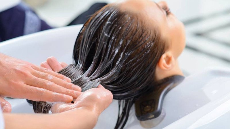 Chai dầu xả và người phụ nữ đang xả tóc, minh họa cách chăm sóc tóc nhuộm đúng cách