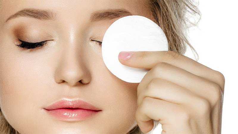 Cô gái dùng bông tẩy trang làm sạch da mặt trước khi ngủ, nhấn mạnh tầm quan trọng của việc chăm sóc da ban đêm để da dễ thẩm thấu dưỡng chất.