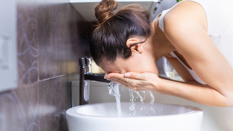 Đôi bàn tay đang vốc nước để rửa mặt, tượng trưng cho việc sử dụng nước ấm để làm sạch da một cách nhẹ nhàng.