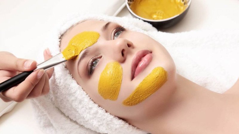 Hỗn hợp sữa chua và tinh bột nghệ màu vàng cam trong bát, với một chiếc thìa nhỏ