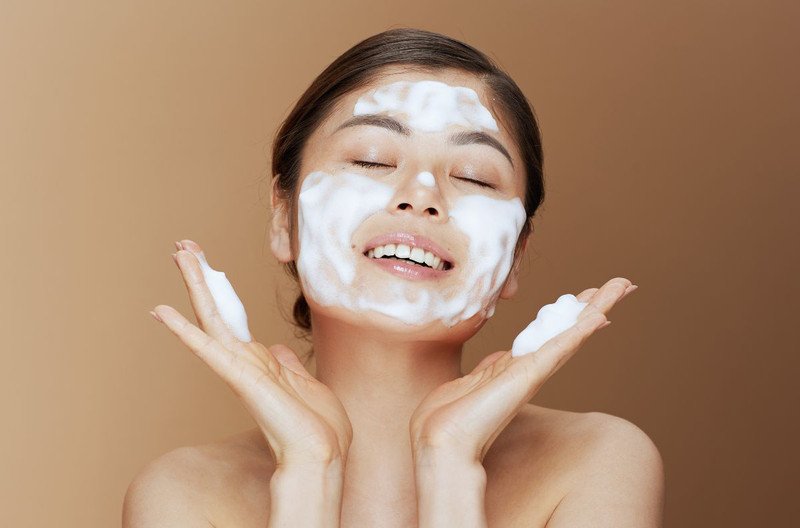 Người phụ nữ đang đọc thông tin về các loại sữa rửa mặt, thể hiện sự tìm kiếm giải pháp cho da dầu mụn