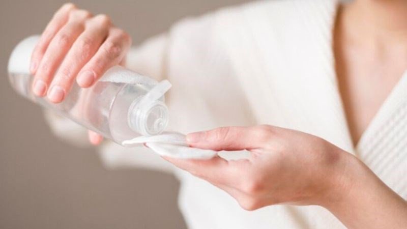 Người phụ nữ đang tẩy trang bằng bông và dung dịch, thể hiện sự cần thiết của việc làm sạch da mặt.