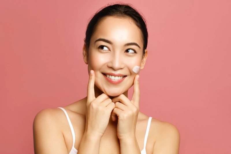 Người phụ nữ đang thoa kem chống nắng lên mặt sau khi chăm sóc da, nhấn mạnh tầm quan trọng của việc bảo vệ da