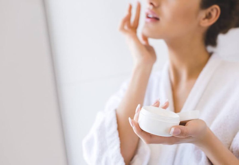 Người phụ nữ nhẹ nhàng thoa kem dưỡng ẩm lên mặt, biểu trưng cho việc chăm sóc da đúng thời điểm giúp hấp thu dưỡng chất tối ưu.