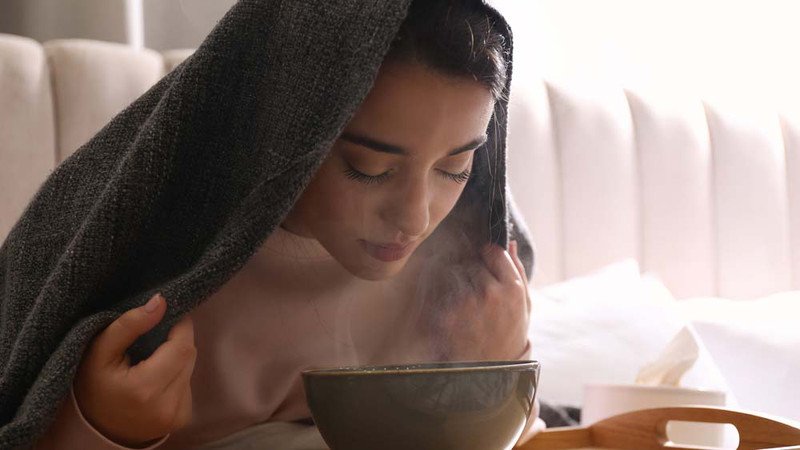 Người phụ nữ trùm khăn để hơi nước xông mặt tập trung hiệu quả